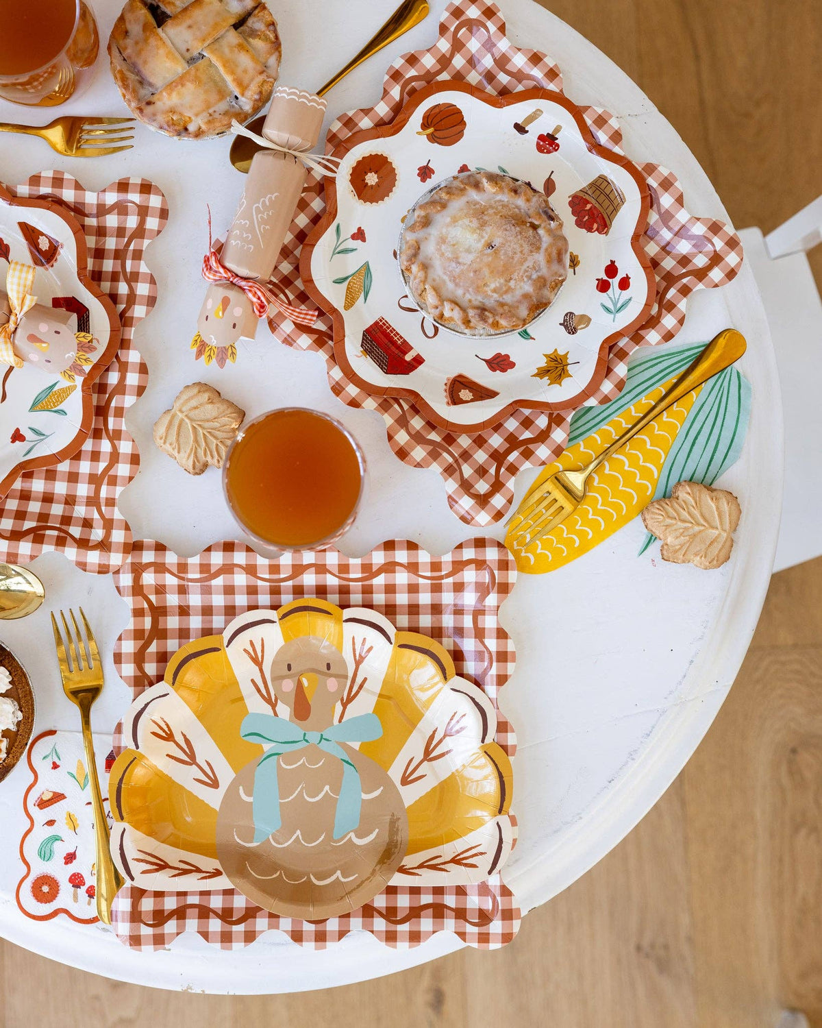 A closer view of a decorative Thanksgiving table setting with gingham charger plates, fall themed paper plates, napkins, and cutlery on a wooden table.