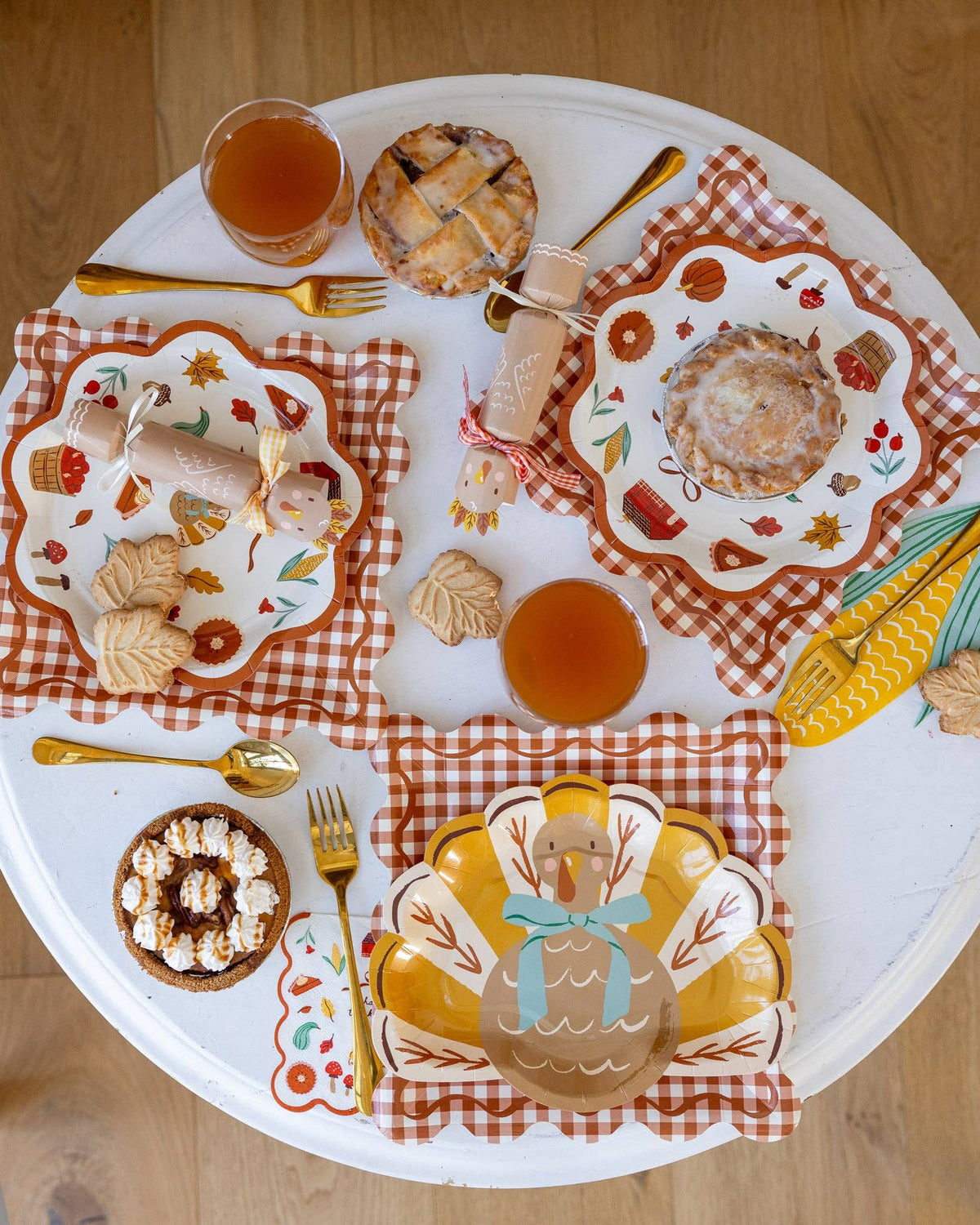 Decorative Thanksgiving table setting with turkey gobble paper plates, charger plates, festive crackers, cutleries, pies, and drinks on a round table.
