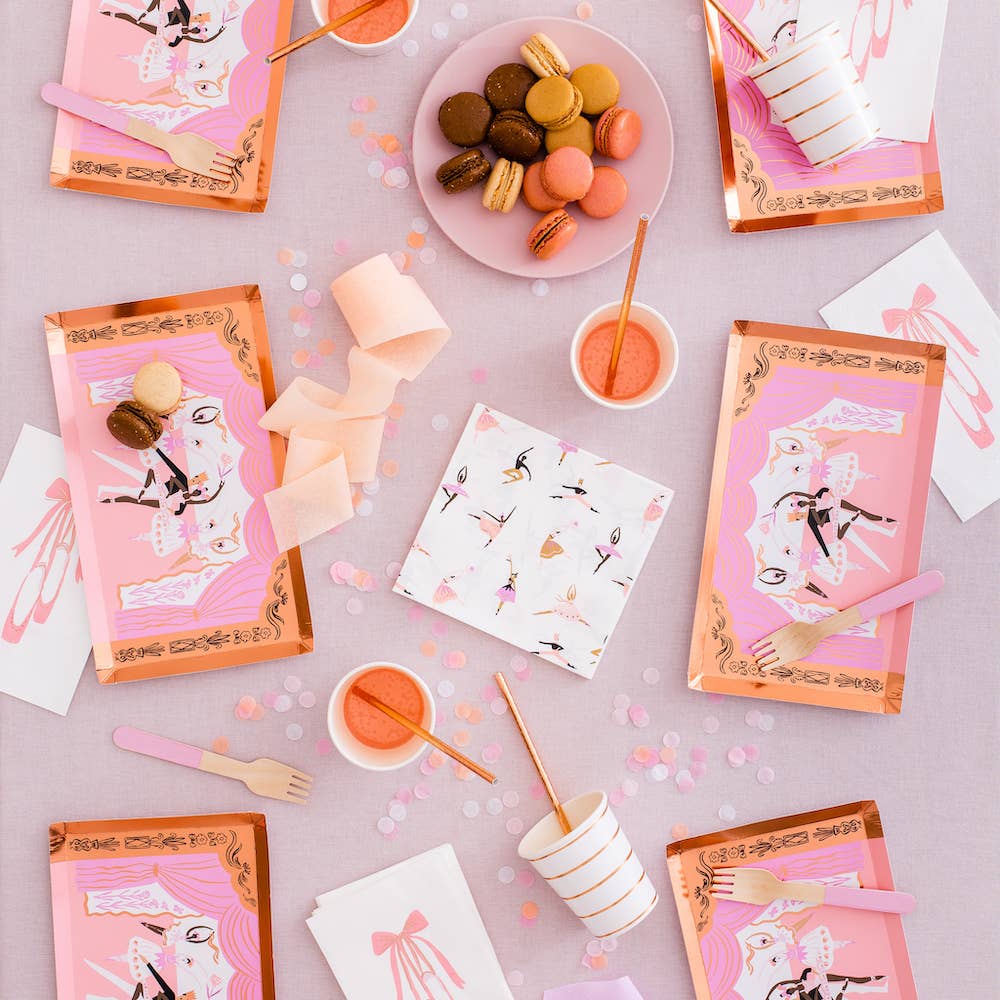 Top-down view of a pink ballet themed party table with macarons, gold striped cups, and ballerina napkins.