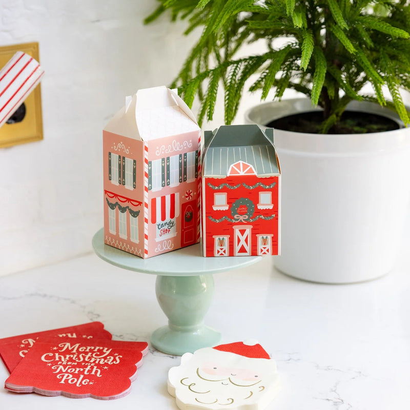 Two assembled Christmas cookie boxes displayed on a small cake stand, alongside matching paper goods.