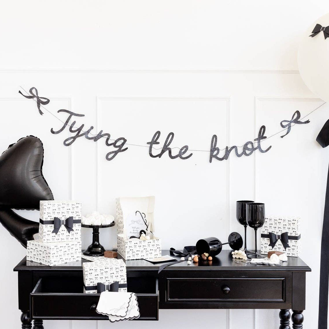 Black glitter Tying the Knot banner displayed over black dessert table with party décor