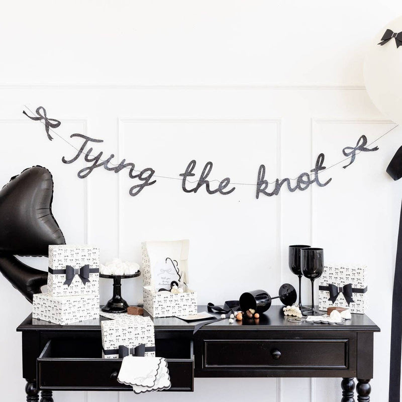Black glitter Tying the Knot banner displayed over black dessert table with party décor