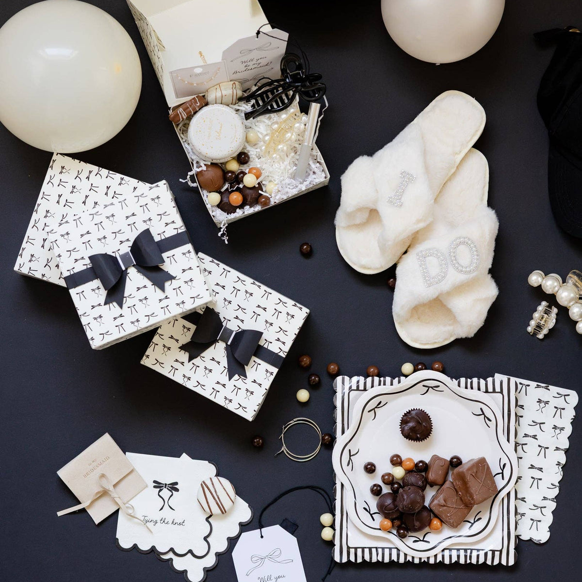 Flat lay of Tying the Knot gift setup with slippers, sweets, bow napkins, and treat boxes.