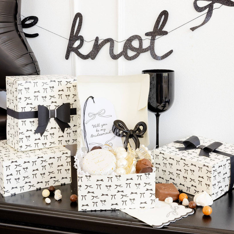 Styled Tying the Knot Treat Box filled with chocolates and party treats on a black table.