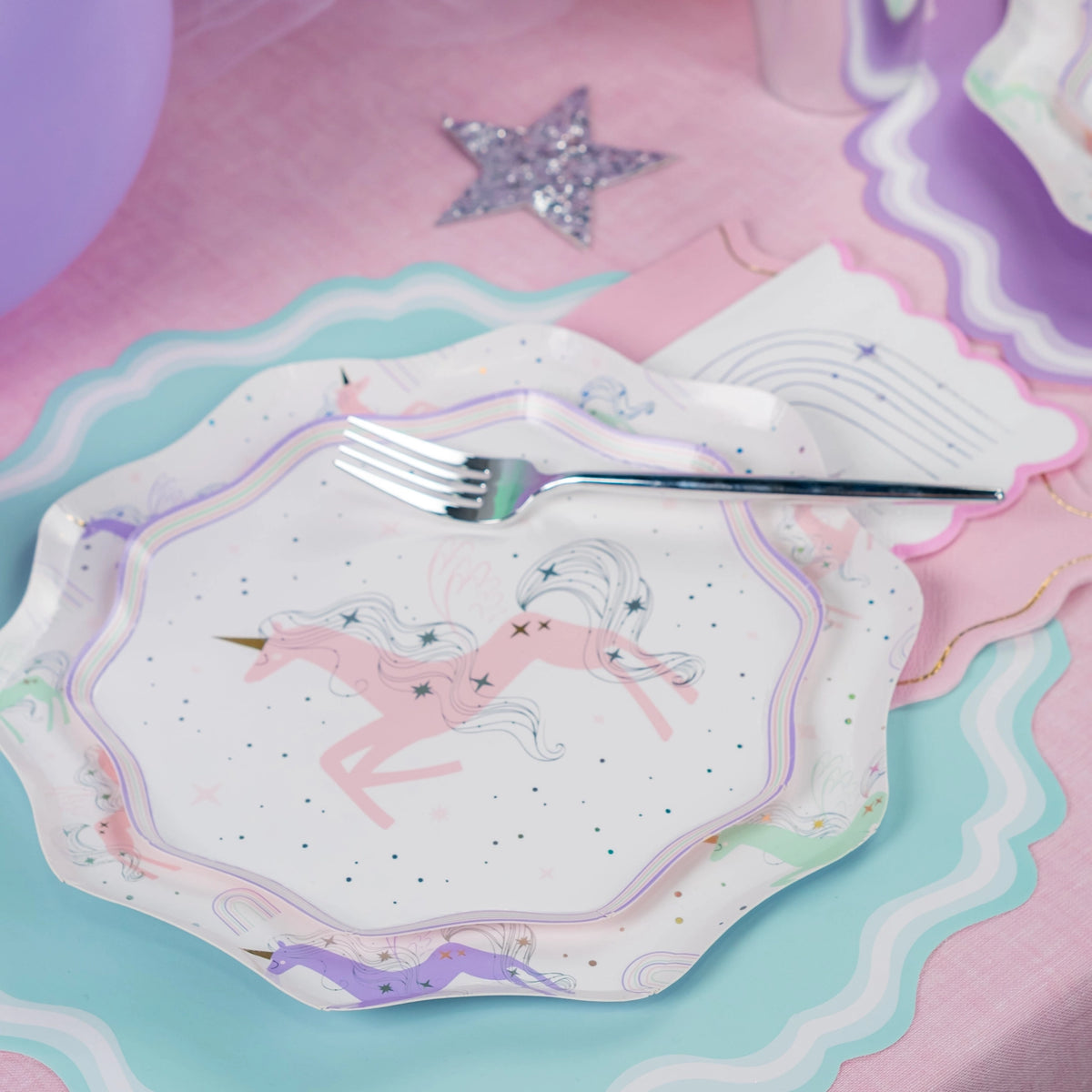 Close shot of pink unicorn plate layered over mint charger and rainbow napkin.
