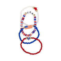 Flat lay of four patriotic beaded bracelets arranged overlapping on a white background showing USA letter beads, flag charm, and star details