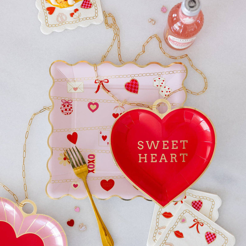 Valentine charm scalloped plate styled with red heart plates, gold utensils, and matching Valentine napkins.