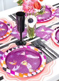 Vertical tablescape view of a modern adult Halloween party with the purple Midnight Spirits plates paired with black champagne flutes.