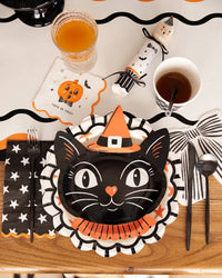 Retro Halloween place setting with a black cat shaped plate, striped scalloped charger, cat cocktail napkin and black flatware