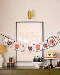 Halloween-themed party setup with vintage character banner and other decorations, cake, and treats on a table.