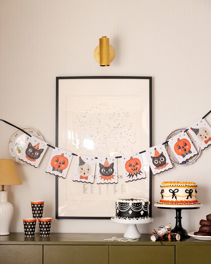 Halloween-themed party setup with vintage character banner and other decorations, cake, and treats on a table.