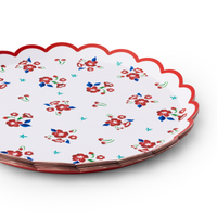 Angled close-up of stacked vintage floral scalloped paper dessert plates showing red flowers, blue leaves, cherry motifs, and red scalloped edge
