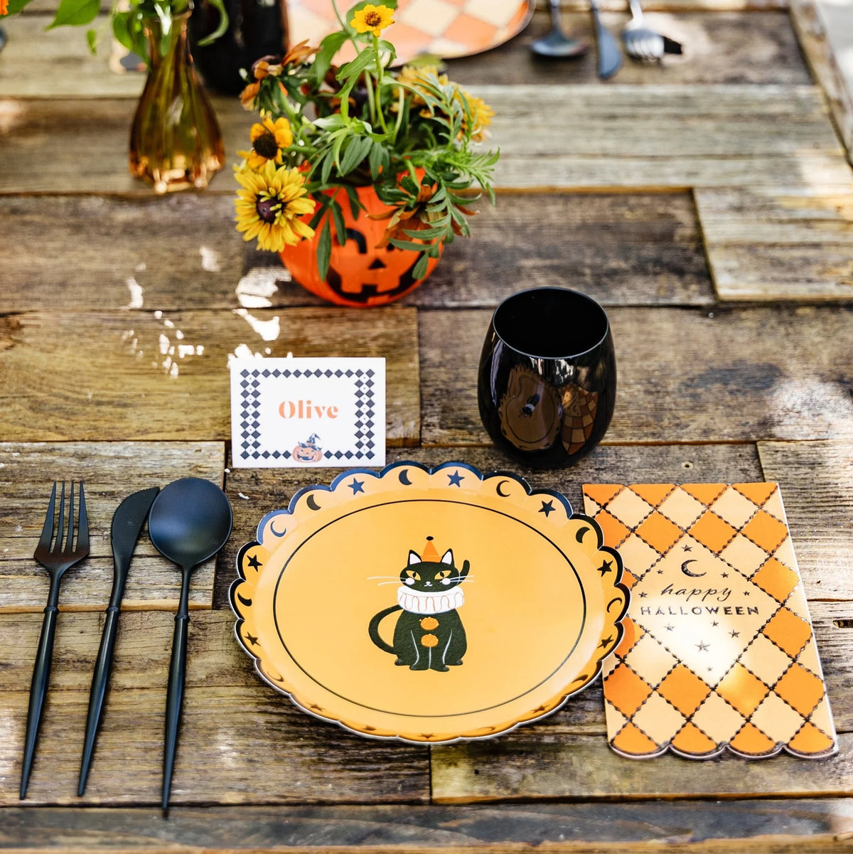 Wood-table place setting with a black cat vintage Halloween plate, black flatware, and an orange gingham napkin.