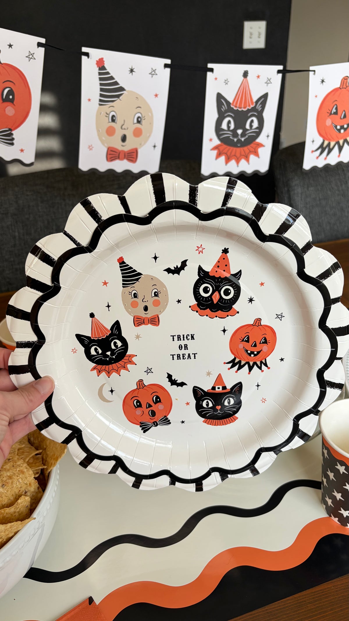 Vintage Halloween character paper plate with cats, owls, and pumpkins on a table layered with a black scalloped charger, star cups, and the character banner in the background