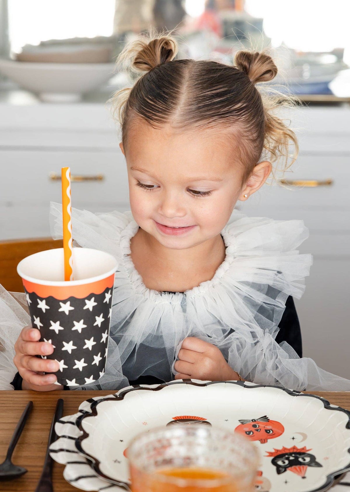 Young girl with pigtails sitting at a table with a Halloween-themed plate and vintage halloween star cup.