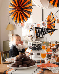 Halloween-themed party with decorations, a child, and a cake with a Trick or Treat felt pennant.