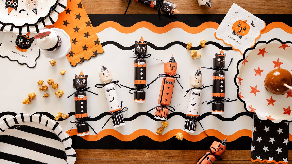 Halloween-themed table setting with decorative party crackers and pumpkins on a wooden table.