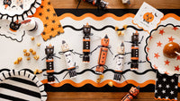 Halloween-themed table setting with decorative party crackers and pumpkins on a wooden table.
