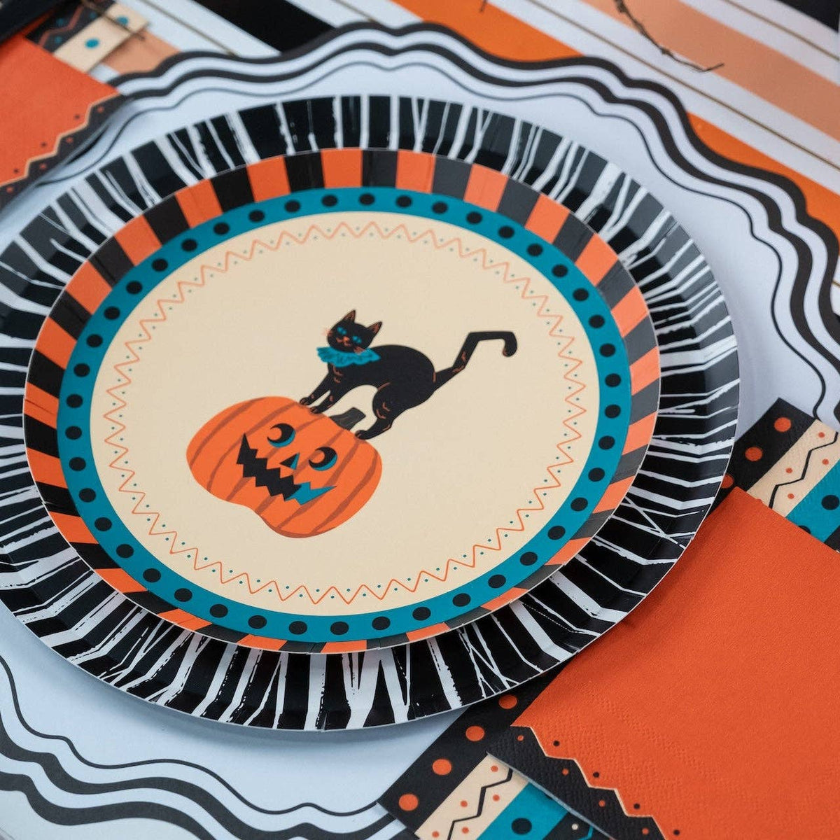 Styled vintage Halloween place setting with the cat plate, black fringe charger, orange napkin, and black flatware from an angle.