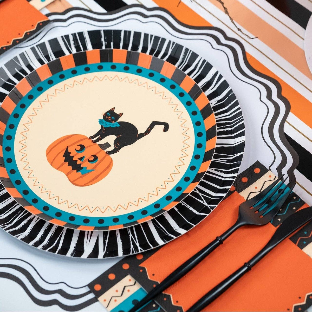 Styled vintage Halloween place setting showing the cat-and-pumpkin plate on a black fringe rosette charger with orange napkins and black flatware on a striped runner.