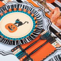 Styled vintage Halloween place setting showing the striped guest towel with a black cat-and-pumpkin plate on a black fringe charger and orange napkins on a striped runner.