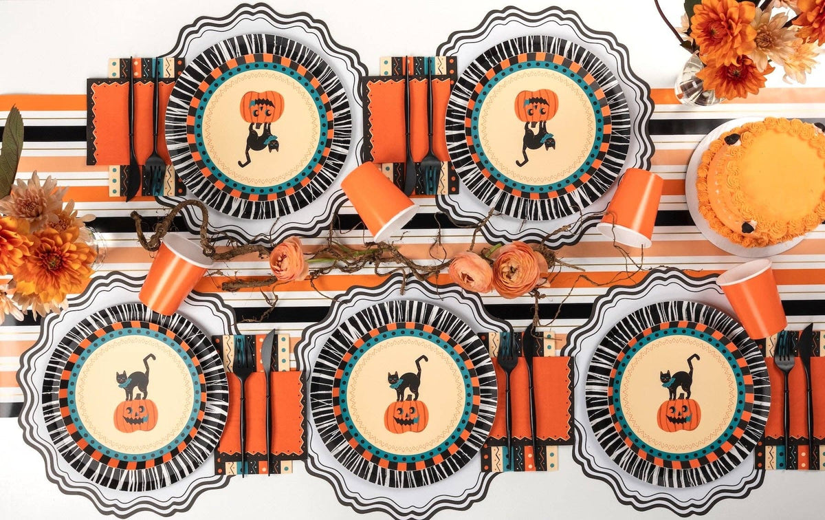Overhead Halloween table with vintage cat plates, retro striped towels, orange cups, and striped runner across settings.
