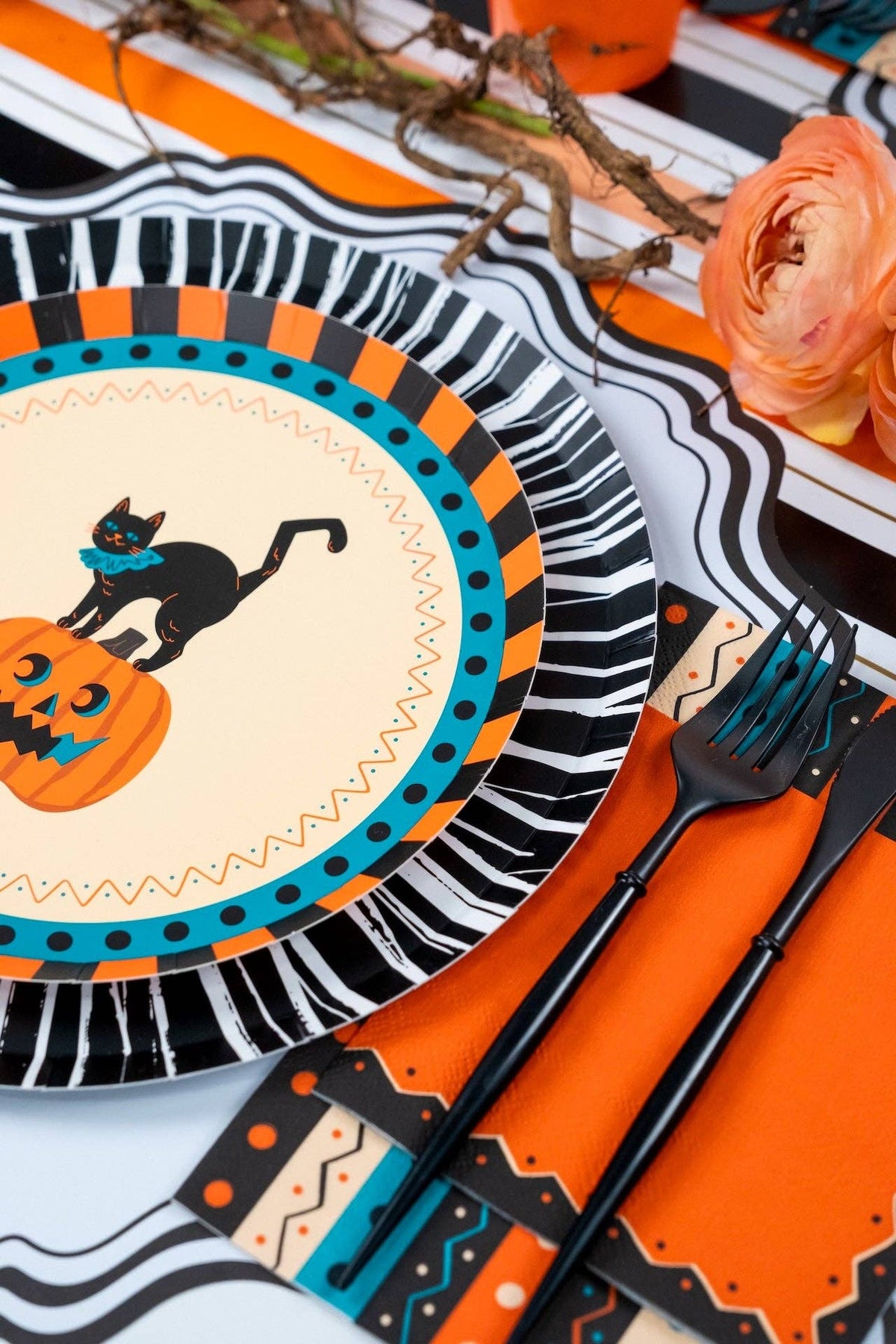 Overhead Halloween tablescape — multiple vintage cat plates, orange napkins, orange cups, and black-and-cream striped runner with fall florals.