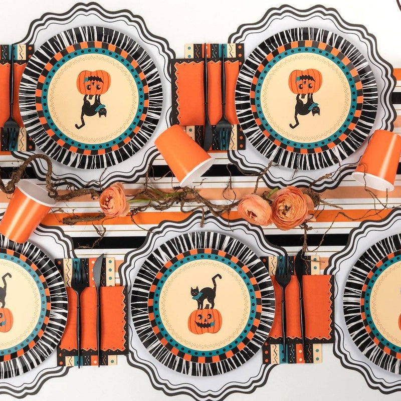 Overhead Halloween tablescape — multiple vintage cat-and-pumpkin plates on black rosette chargers, orange ribbon accents, and fall florals on a striped surface.
