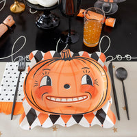 Halloween table setting with harlequin dinner plate used as a charger under a pumpkin plate, black goblet, and treats.