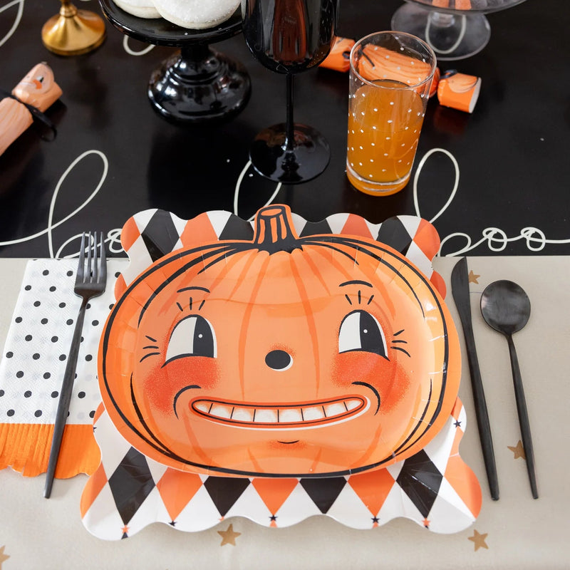 Halloween table setting with harlequin dinner plate used as a charger under a pumpkin plate, black goblet, and treats.