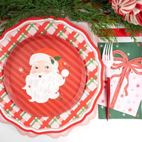 Overhead place setting featuring a vintage Santa plate on a red plaid charger with the pink present napkin and a red fork.