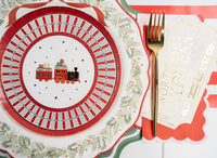 Place setting with a vintage red-train plate, holly rim, green scalloped charger, gold fork, and a cream guest towel with gold lettering.