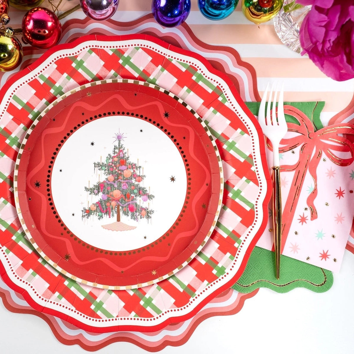 Overhead view of a festive place setting featuring a vintage Christmas tree plate on a plaid charger with the pink present napkin.
