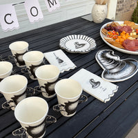 Overhead witch party table with cream cauldron cups, black witch-hat plates, Welcome Witches napkins, and orange snacks