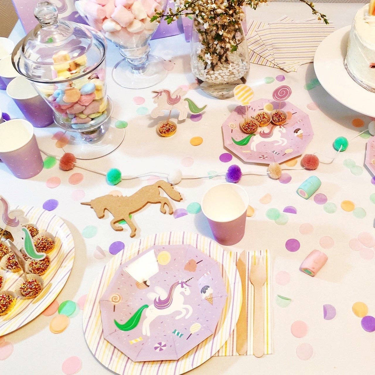 Full party table spread with unicorn plates, treats, and pastel decorations