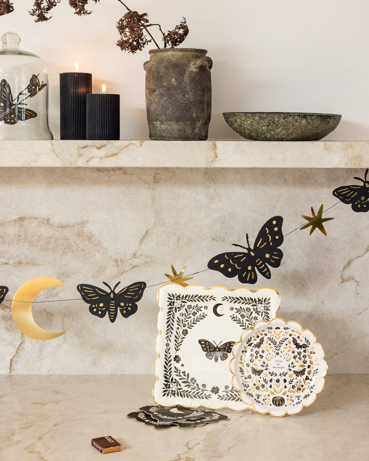 Styled autumn mantel display featuring stacked moonlight moth square plates alongside dark taper candles and celestial moth decor.