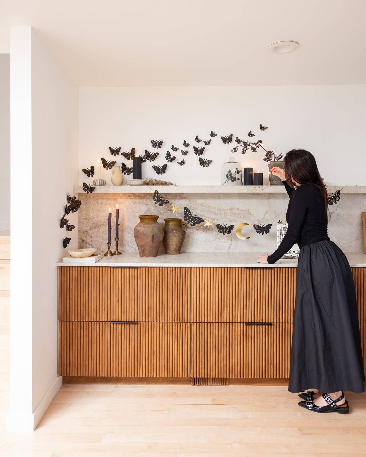 Wide angle view of a moody autumn living room setup featuring the celestial moth paper banner draped across a wooden cabinet and marble shelf display.