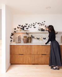 Wide angle view of a moody autumn living room setup featuring the celestial moth paper banner draped across a wooden cabinet and marble shelf display.