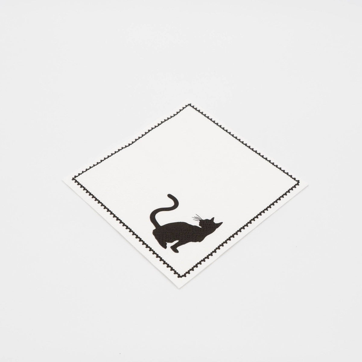 Angled studio view of the black cat silhouette paper cocktail napkin partially unfolded, showing the printed design.