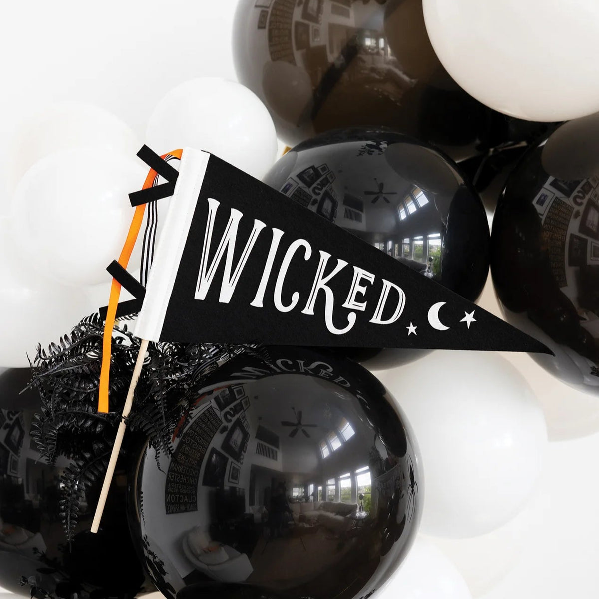 Hand holding black WICKED felt Halloween flag with moon and stars among balloons.