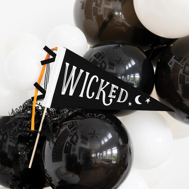 Hand holding black WICKED felt Halloween flag with moon and stars among balloons.