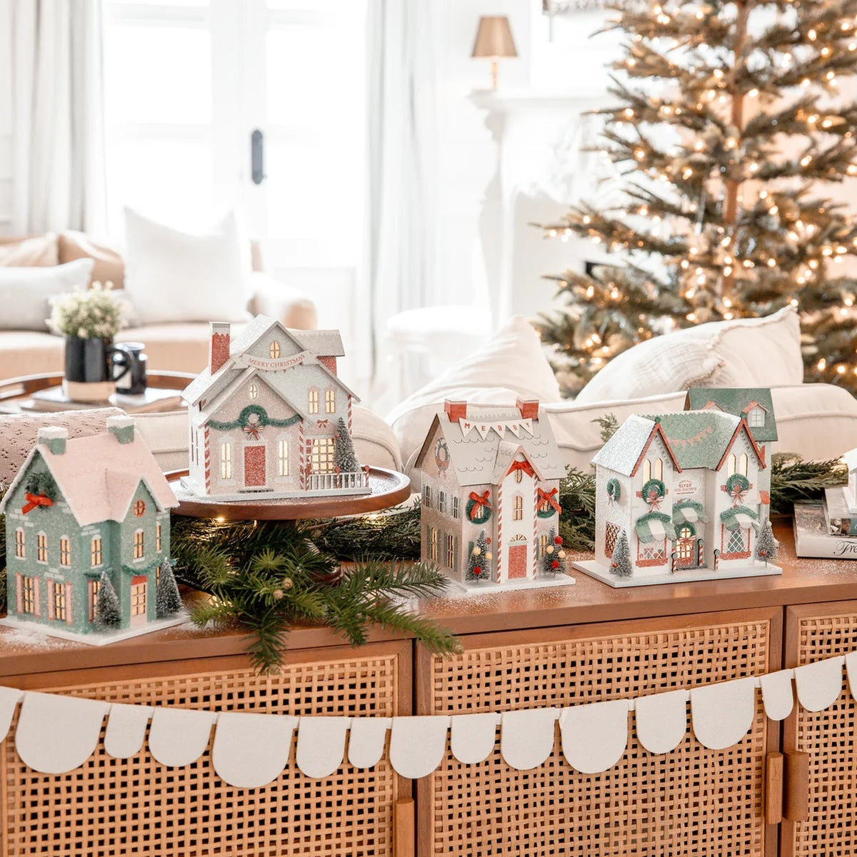 Wide view of a console table displaying the full collection of lighted paper house pieces with a North Pole decor theme.