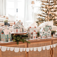 Wide view of a console table displaying the full collection of lighted paper house pieces with a North Pole decor theme.