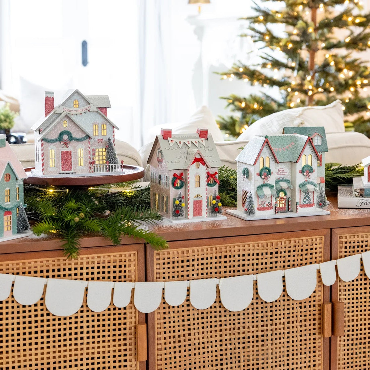 Wide shot of the full Christmas village collection set up on a console table with holiday greenery.