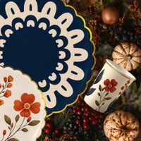 Wildflower cup on its side among navy doily and wildflower plates, berries, and speckled pumpkins