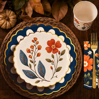Fall place setting with wildflower plates on a rattan charger, a floral cup, and a navy napkin with gold flatware