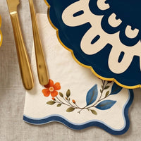 Wavy edge wildflower napkin under gold flatware beside a navy doily plate on linen