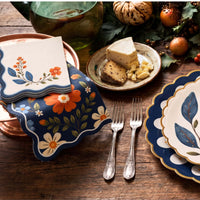 Stack of wavy edge wildflower napkins on a copper tray beside a navy floral guest towel and cheese plate