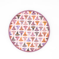 Round witch hat Halloween dessert plate covered in an all-over repeating pattern of colorful patterned witch hats in orange, lavender, blush, and black, with a blush-lavender scalloped edge, overhead flat-lay on white background.