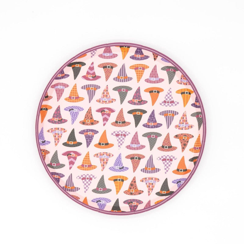 Round witch hat Halloween dessert plate covered in an all-over repeating pattern of colorful patterned witch hats in orange, lavender, blush, and black, with a blush-lavender scalloped edge, overhead flat-lay on white background.